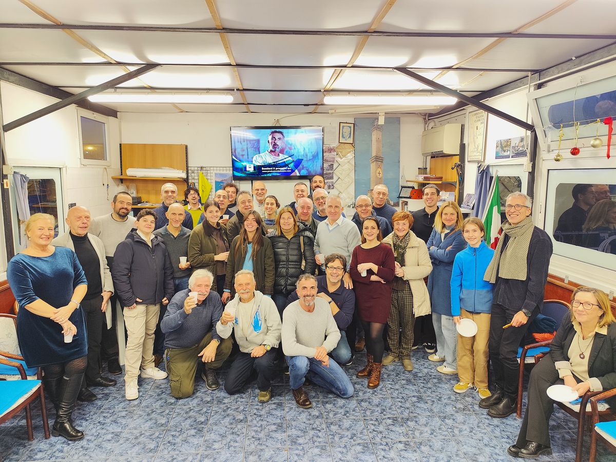 gruppo di persone socie del Centro Sub Med “Duilio Marcante” intente a fare gli auguri rivolte verso la fotocamera, all'interno della sede, la Chiatta aragostiera, la Gaiazza, presso il porto antico di genova