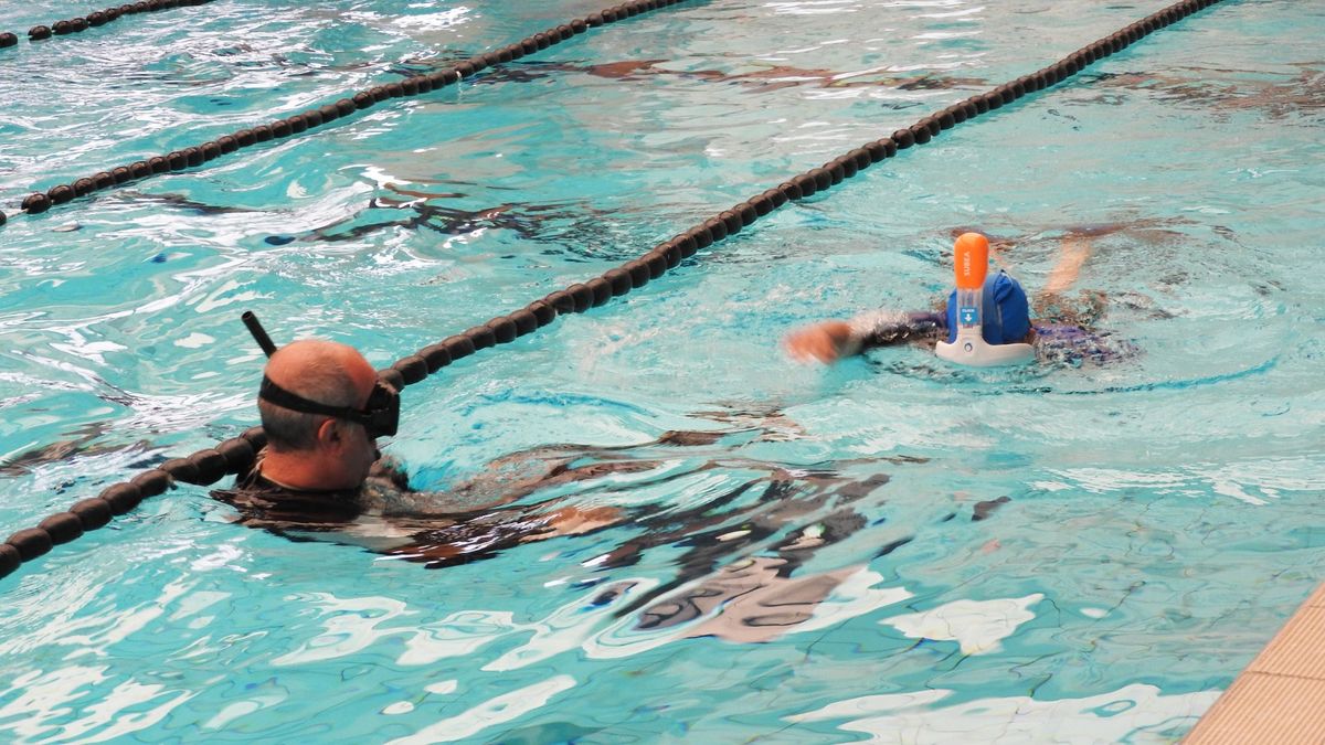 sessione in piscina ripresa da bordo vasca con istruttore che osserva allievo o allieva con maschera intenta a guardare sott'acqua